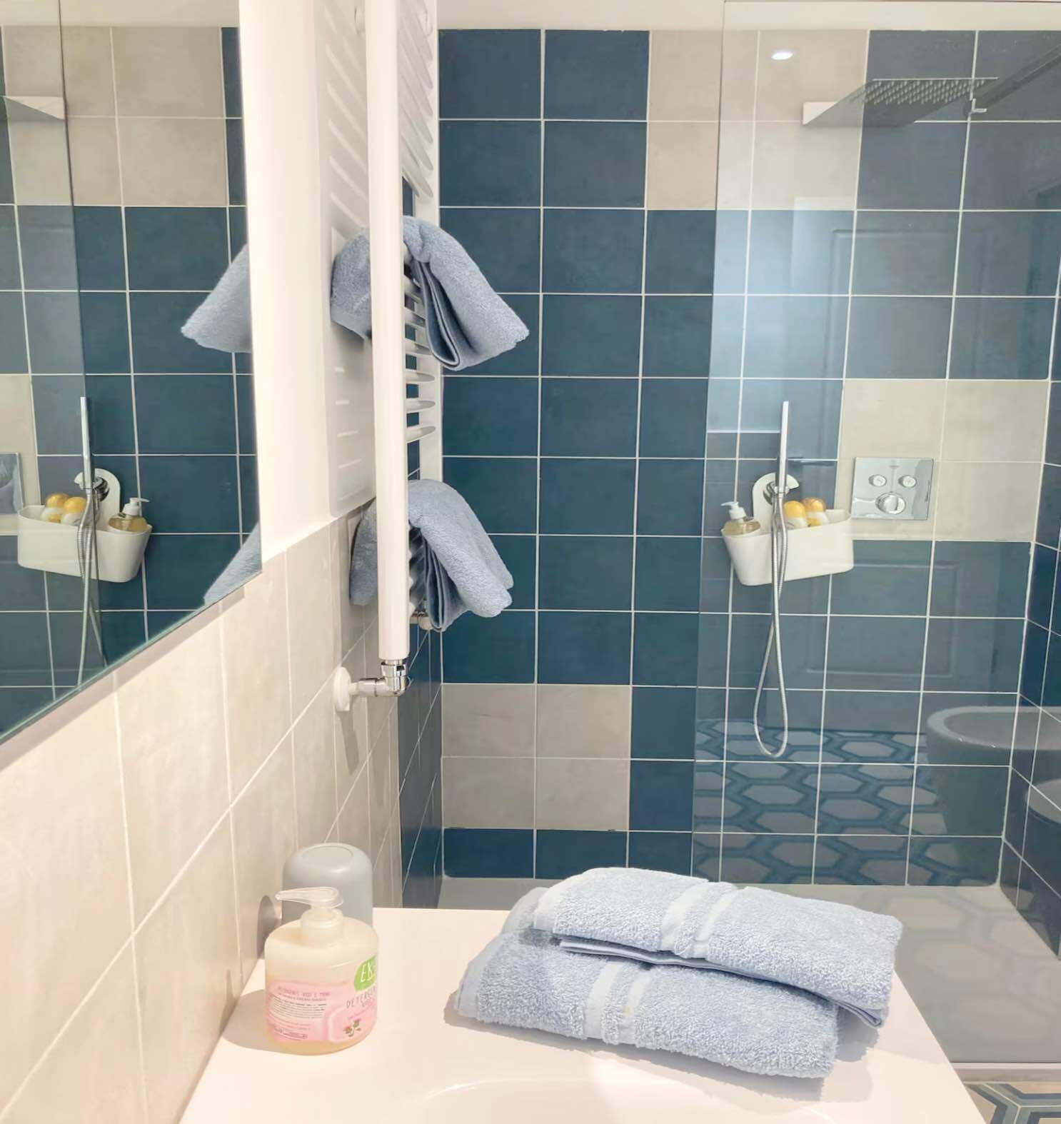 A bathroom with blue and white tiles, a towel rack, a shower, and toiletries on the counter.