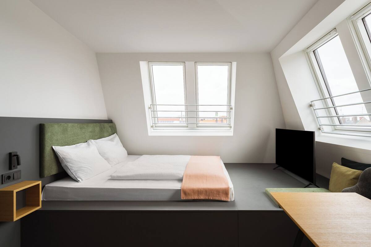 Une petite chambre comprenant un lit, un bureau, une télévision et une fenêtre.