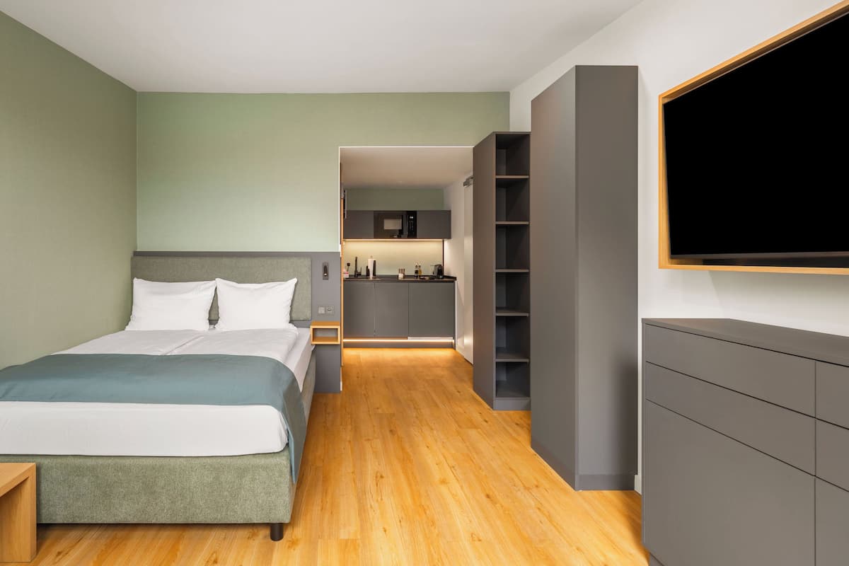Une chambre d’hôtel moderne équipée d’un lit, d’une télévision, d’une kitchenette et d’un plancher en bois.