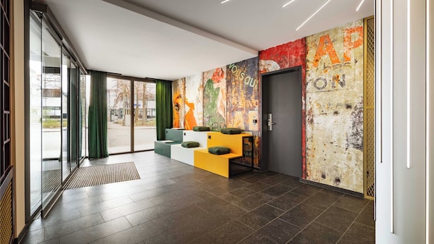 A modern lobby with a glass door entrance, a seating area with cushions, and a colorful mural on the wall. - Limehome Munich Theresienwiese (Munich)