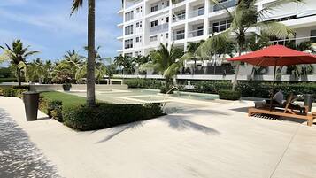 A modern hotel with a pool area, palm trees, and a red umbrella.
