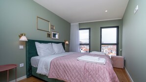 Ein Schlafzimmer mit einem Bett, Nachttischen, einem Fenster und Blick auf Gebäude.