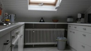 Pieni, käytännöllinen keittiö, jossa on kattovalokuvio, valkoiset kaapit, patteri ja roskakori.