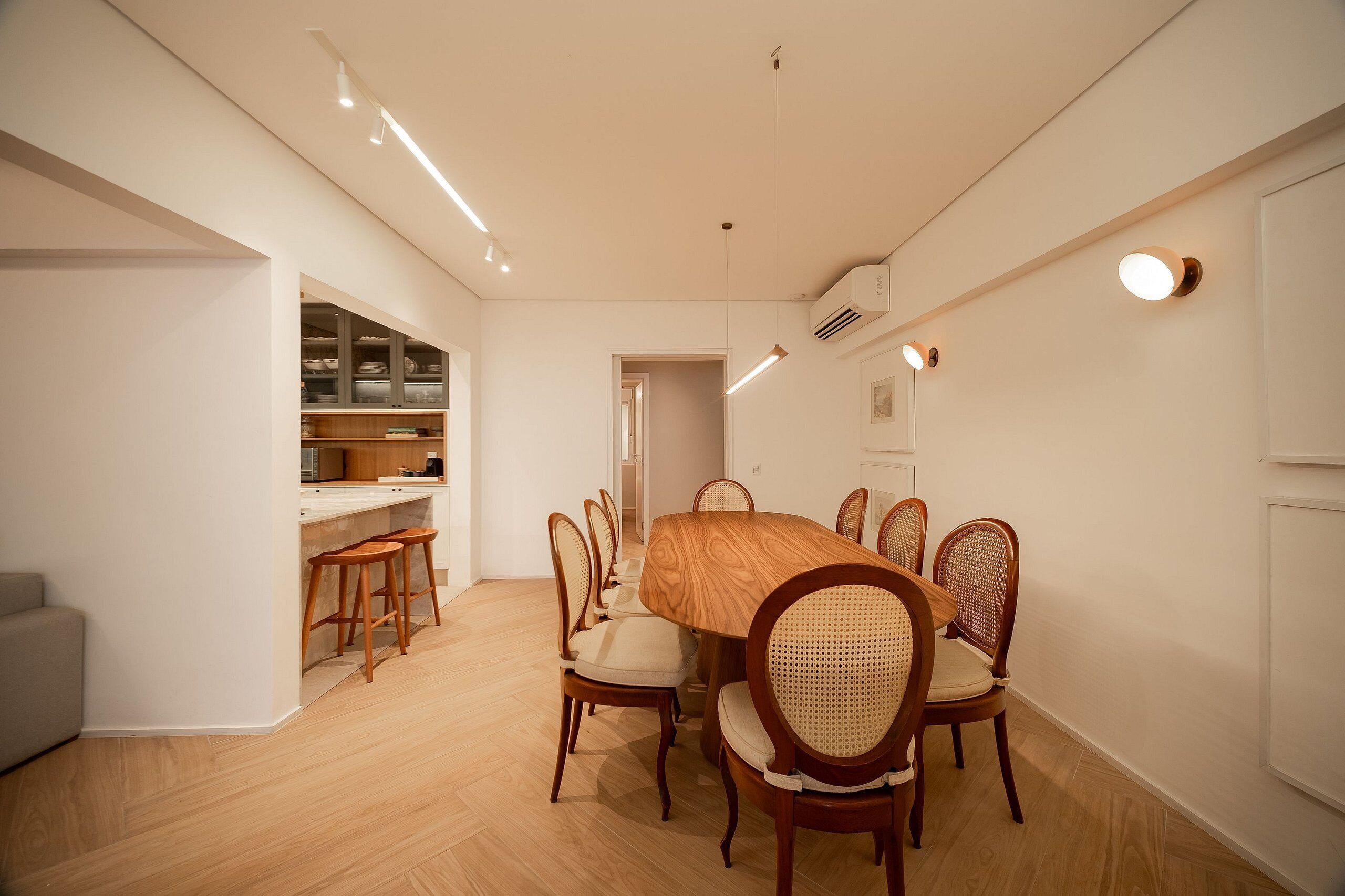 Un comedor con una mesa y sillas de madera, una cocina con armarios y una pared blanca con una lámpara.