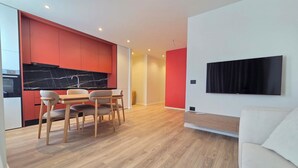 A modern kitchen with red cabinets, a black marble backsplash, and a dining area with wooden chairs and a table. - Joanna Prestige Apartments (Sarande)