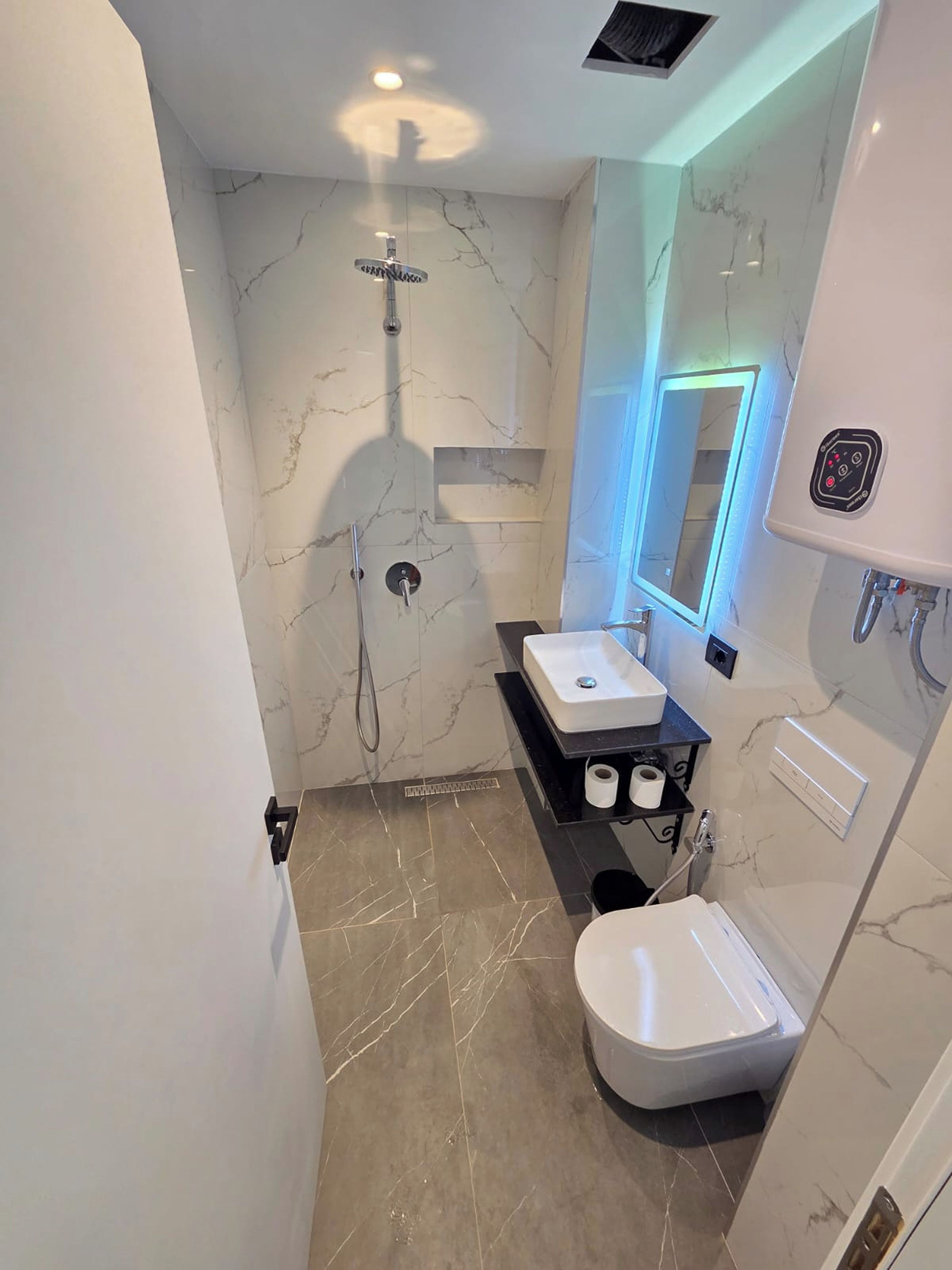 Un baño moderno con ducha de mármol, lavamanos, inodoro y espejo.