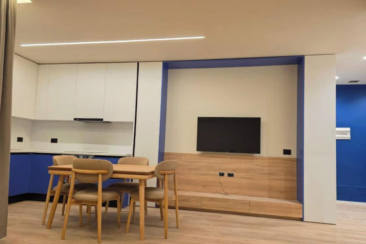 Una cocina moderna con armarios blancos, encimera de madera y televisor de pantalla plana montado en la pared.