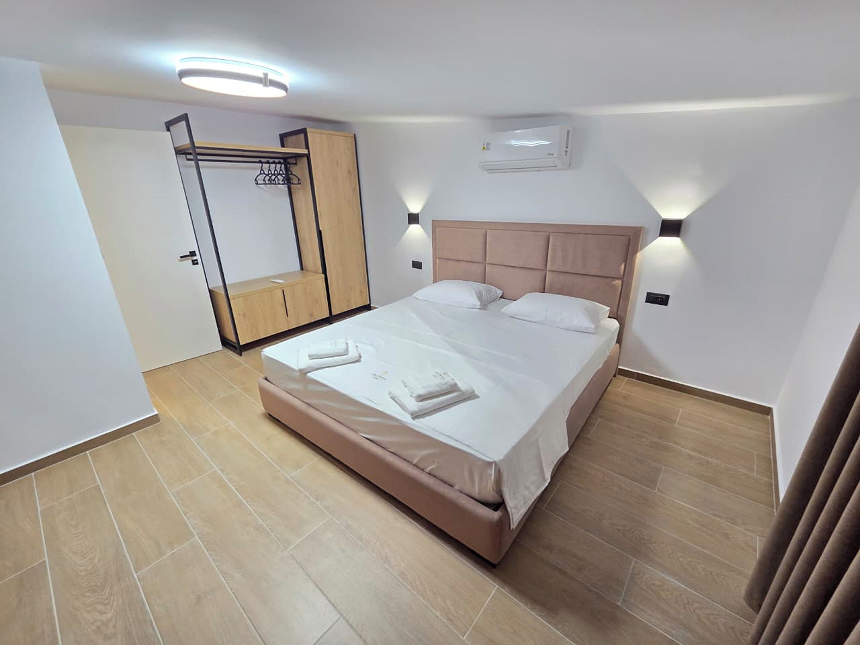 Un dormitorio con cama, lámparas de noche, armario y aire acondicionado.
