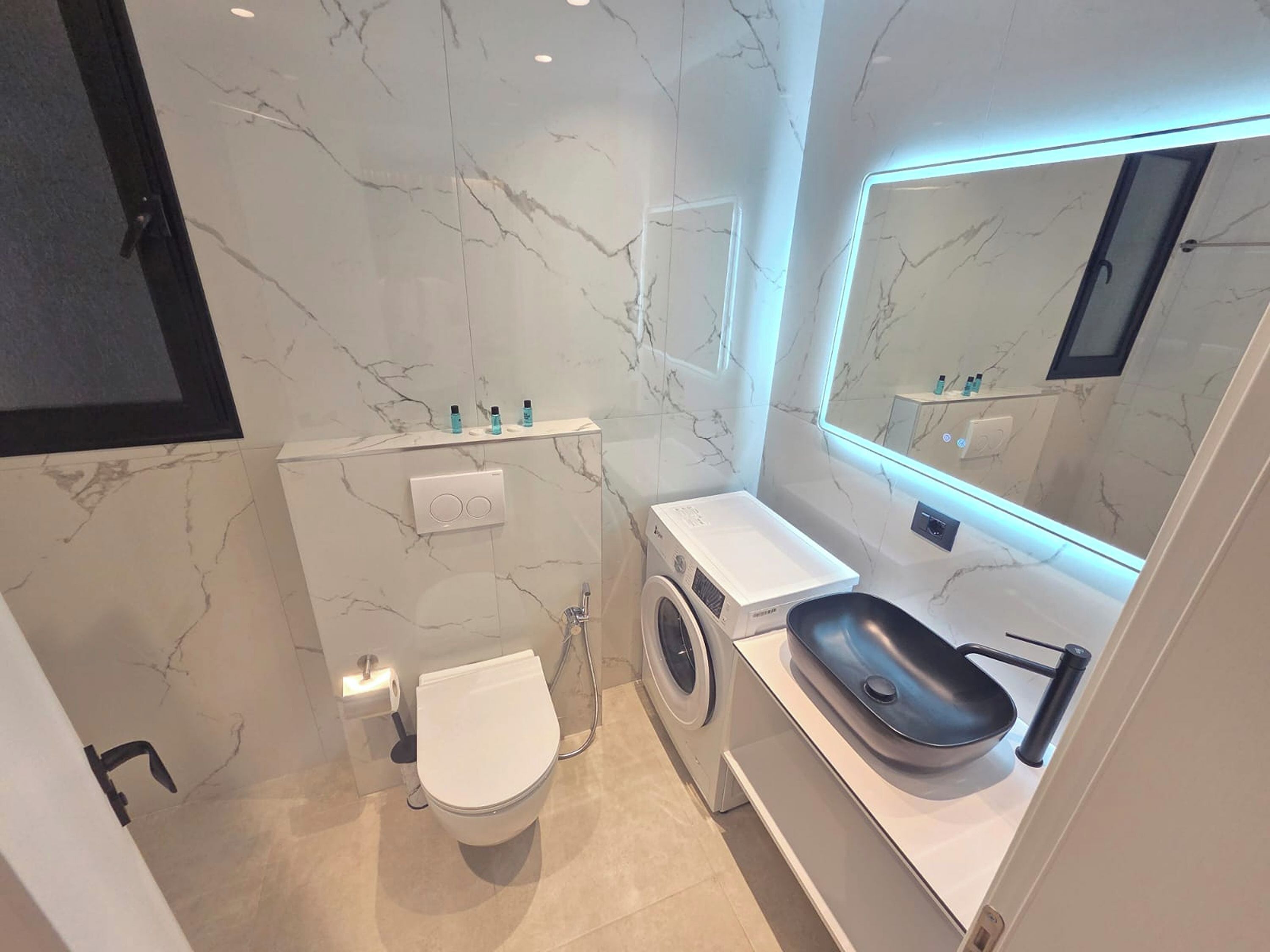 Un baño pequeño con inodoro, lavadora y lavamanos.