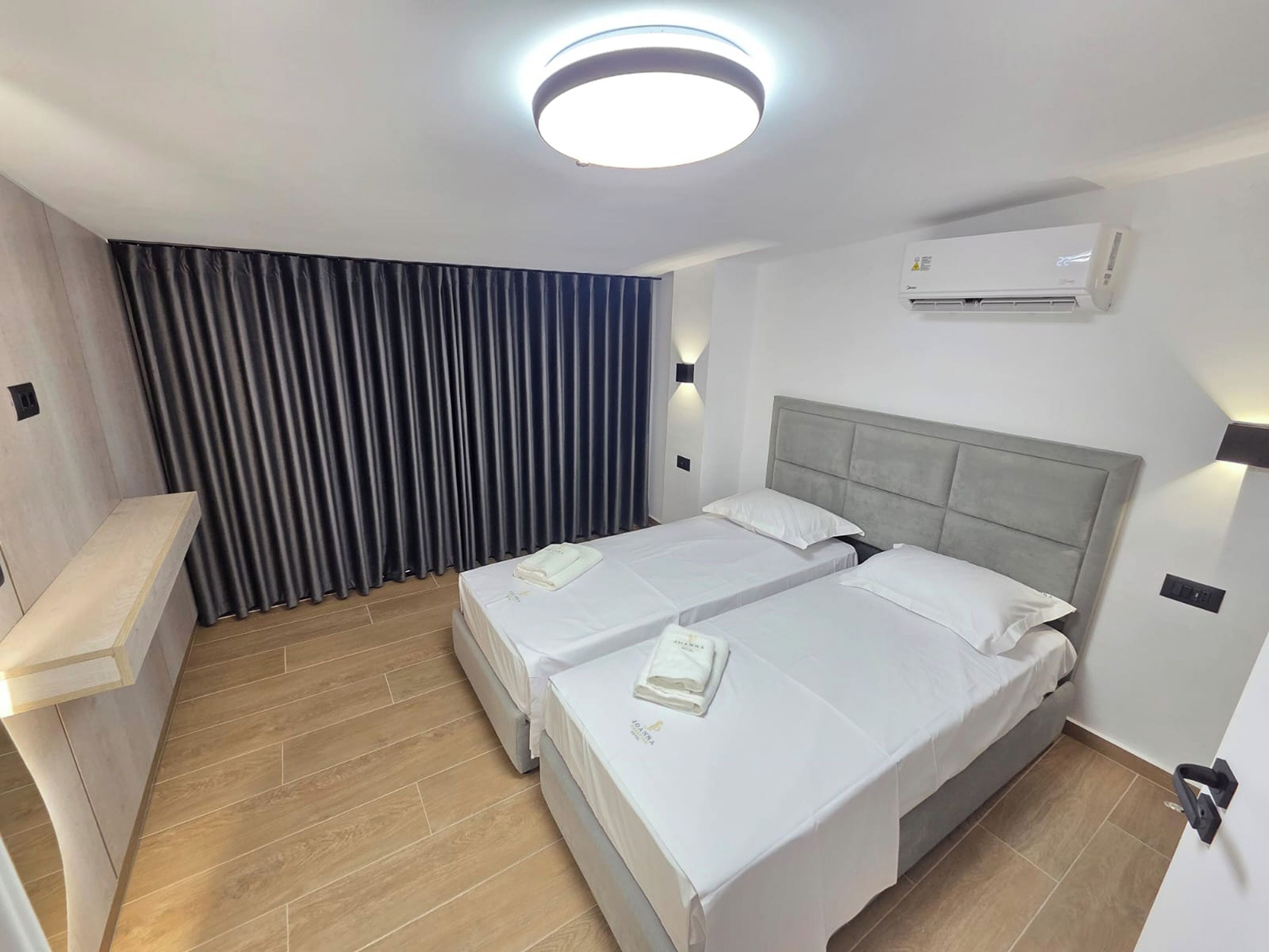 Une chambre d’hôtel avec deux lits, un bureau, un luminaire au plafond, un climatiseur et un rideau.