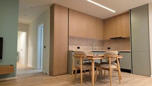 A modern kitchen with wooden cabinets, a dining table with chairs, and a visible sink. - Joanna Prestige Apartments (Sarande)