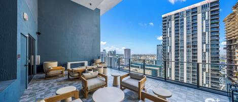 A rooftop lounge with outdoor seating, a city view, and a high-rise building in the background.