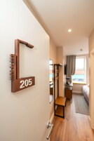 A hallway with a wooden sign indicating room number 205, a bed, a TV, and a window with curtains.