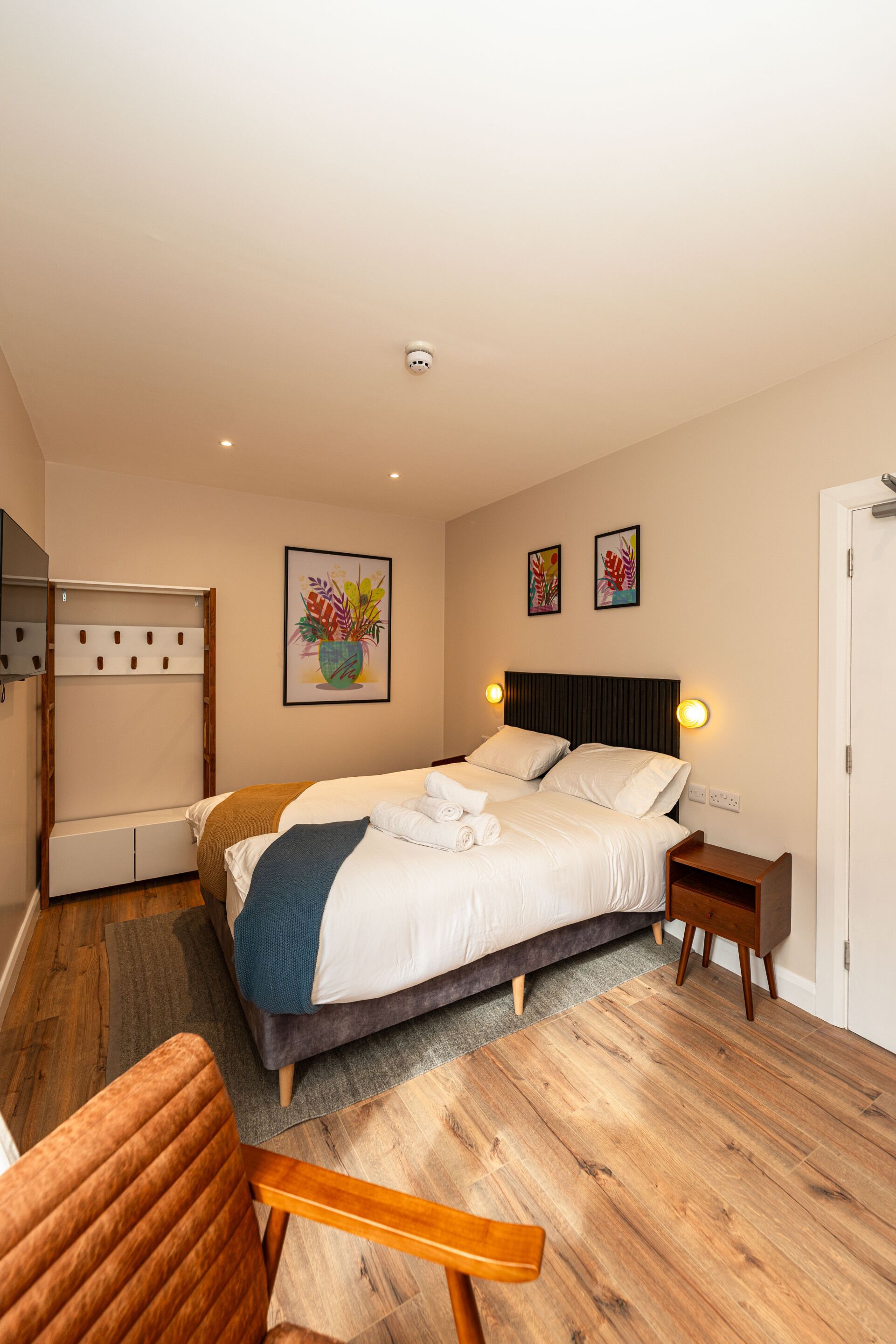 Une chambre à coucher comprenant un lit, des tables de chevet, une armoire, une chaise et des œuvres d’art accrochées aux murs.