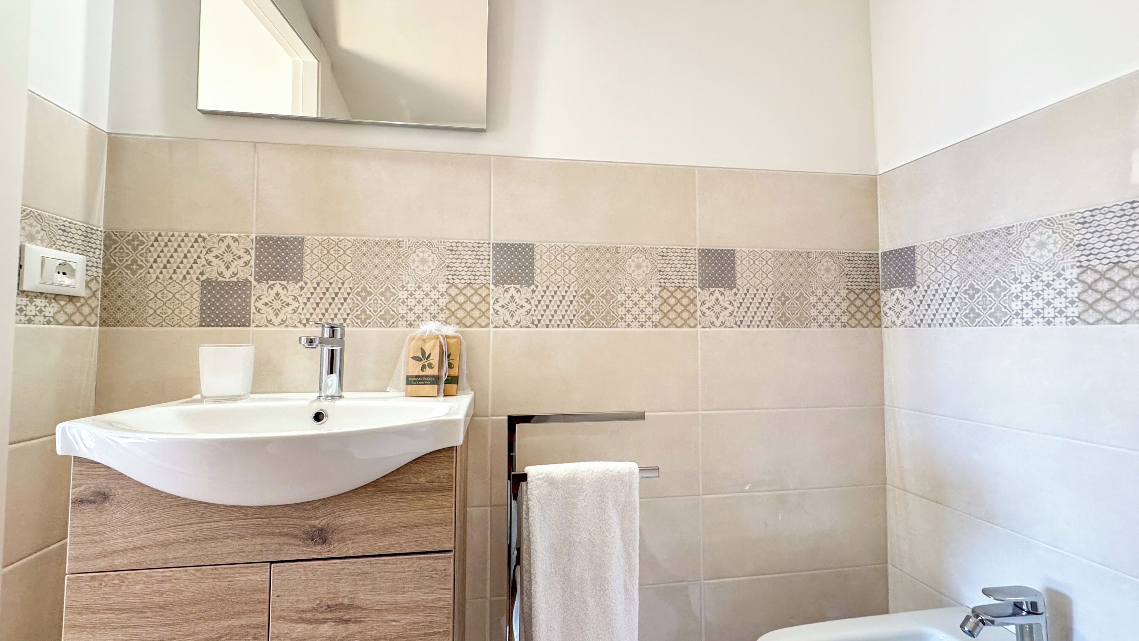 Un baño con lavamanos, espejo, toallero y azulejos estampados.