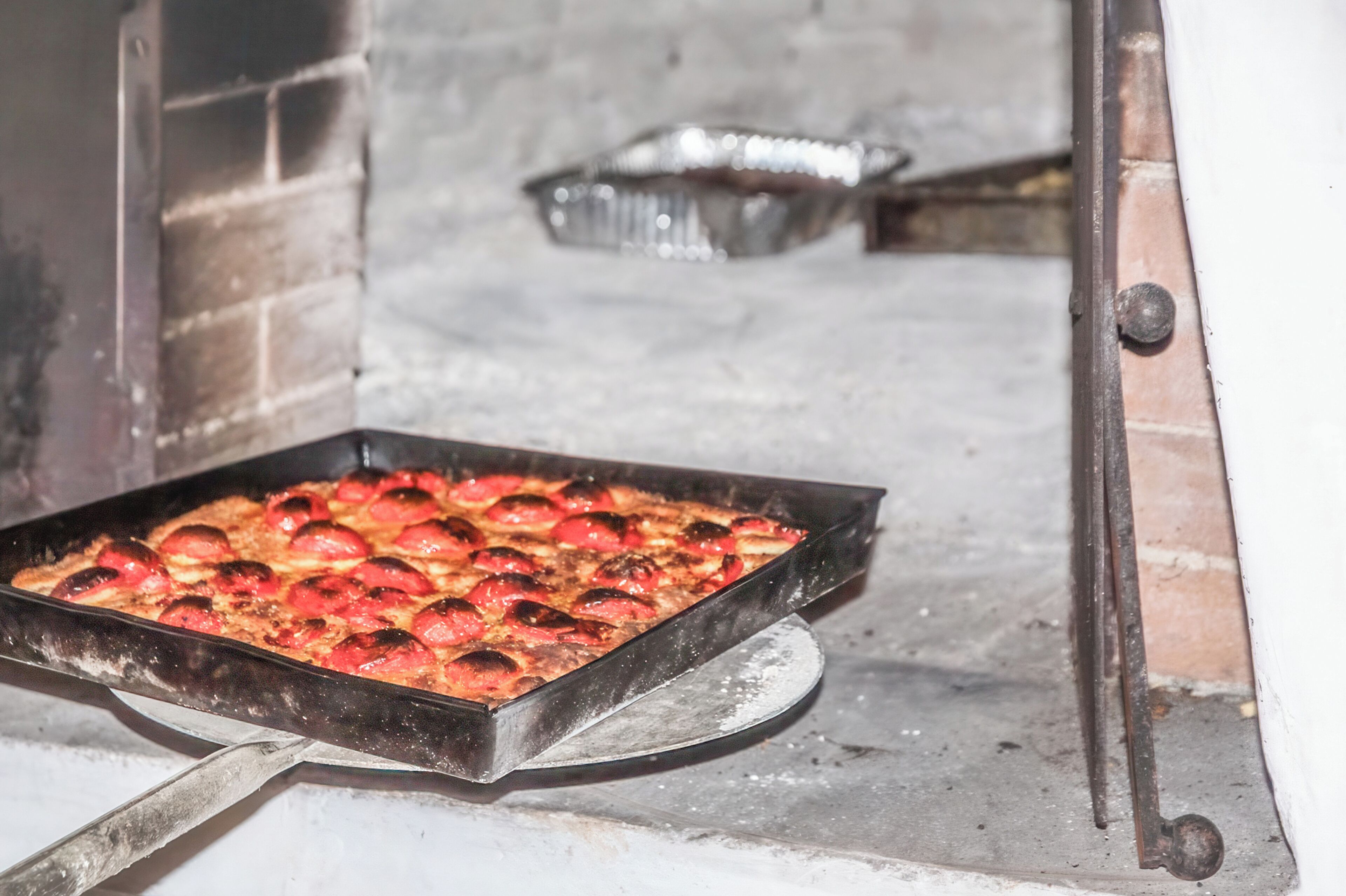 Pizza in einer Metallform in einem Backofen aus Ziegeln.