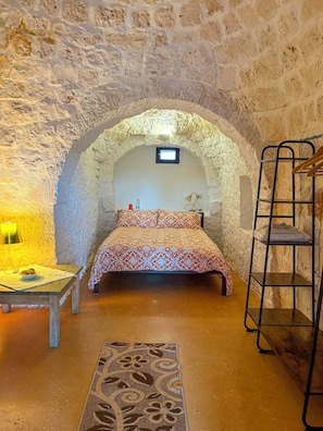 A stone-walled room with a bed, a desk, a lamp, and a shelf. - Borgo di Trulli in Puglia – Ideale per famiglie e gruppi fino a 12 persone (Ceglie Messapica)