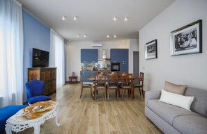 A modern living room with a sofa, a dining table with chairs, a TV, and a kitchen area with cabinets and a stove. - Partenope waterfront (Napoli)