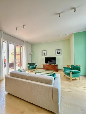 A living room with a sofa, two armchairs, a glass coffee table, a television, and a sliding glass door leading to an outdoor area. - Partenope waterfront (Napoli)