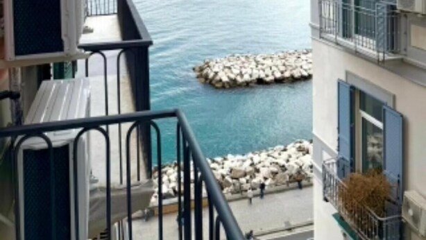 Ein Balkon mit Blick auf das Meer, ein Gebäude mit Balkonen und eine felsige Küstenlinie.