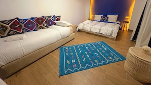 A modern bedroom with a sofa, two beds, a blue patterned rug, and a woven ottoman. - Palais Mahdi (Marrakech)