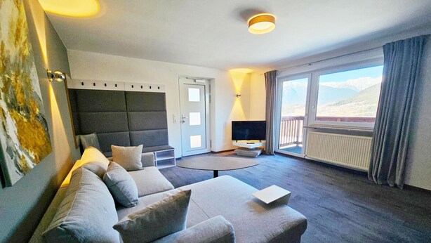 A modern hotel room with a sofa, a flat-screen TV, a small table, and a balcony with a view. - #3 Design Panorama Apartment, BBQ, 6 guests (Arzl)