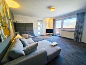 Une chambre d’hôtel moderne dotée d’un canapé, d’une télévision à écran plat, d’une petite table et d’un balcon avec vue.