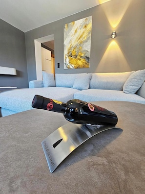 Ein modernes Wohnzimmer mit einem grauen Sofa, einem angebrachten abstrakten Gemälde und einer Flasche auf einem Metallständer.