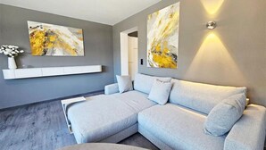 A modern living room with a sectional sofa, a white console table, and abstract wall art. - #3 Design Panorama Apartment, BBQ, 6 guests (Arzl)