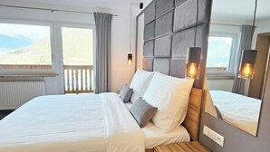 A modern bedroom with a large bed, a wooden nightstand, a mirror, and a view of the mountains. - #3 Design Panorama Apartment, BBQ, 6 guests (Arzl)
