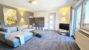 A modern living room with a sectional sofa, a flat-screen TV, and a large abstract painting on the wall. - #3 Design Panorama Apartment, BBQ, 6 guests (Arzl)