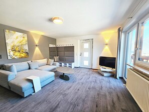 Ein modernes Wohnzimmer mit einer Eckcouch, einem Flachbildfernseher und einem großen abstrakten Gemälde an der Wand.