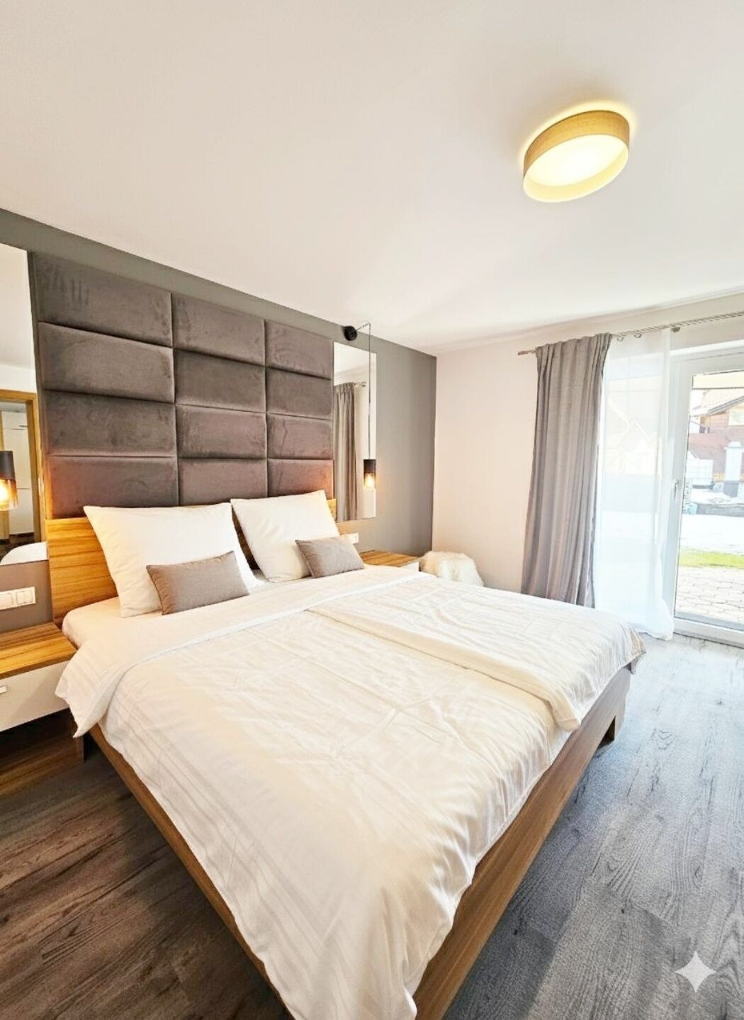 A modern bedroom with a large bed, a headboard, bedside tables, and a window with curtains.