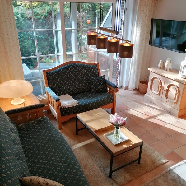 Una sala de estar con sofá, una mesa de centro con un florero, televisor y ventana con cortinas.