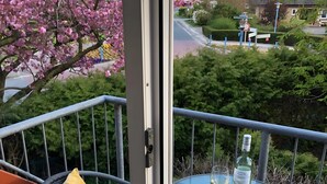 Ein Balkon mit Glastisch, einer Weinflasche und einem Glas Weißwein.