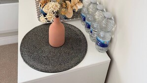 A white table with a vase of flowers, a metal lamp, a white kettle, a red candle, and several water bottles. - Room-charming Double Bedroom With Stunni (Wexford)