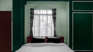 A room with a bed, a window with curtains, a green wall, and a red door. - Super Townhouse Howell Crossway Shillong (Shillong)