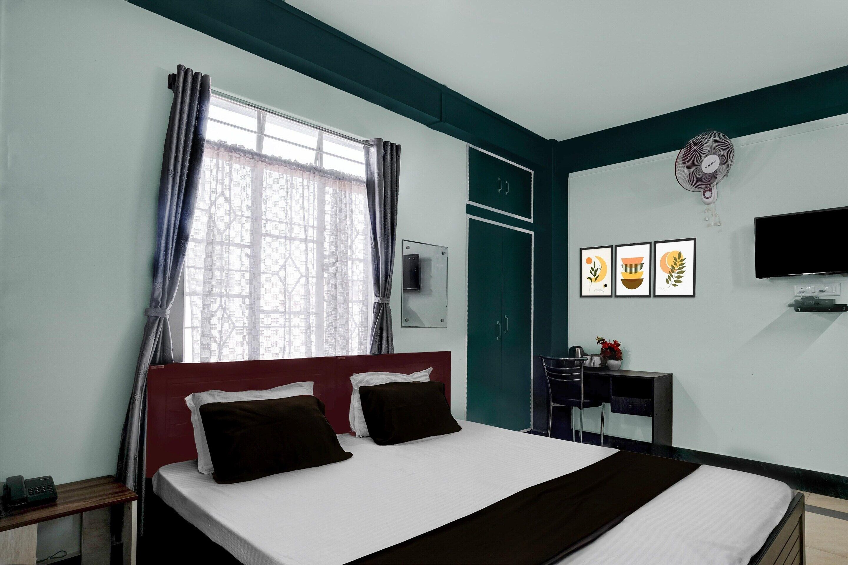 A hotel room with a bed, a desk, a TV, and a window with curtains.