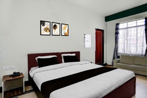 A hotel room with a bed, a nightstand, a window with curtains, and a sofa. - Super Townhouse Howell Crossway Shillong (Shillong)