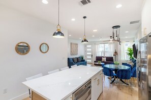 Eine moderne Küche mit Kochinsel, Essbereich mit blauen Stühlen und ein Wohnzimmer mit Sofa.