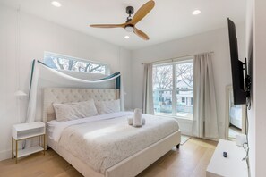 Ein Schlafzimmer mit Bett, Deckenventilator, Fernseher und Fenster.