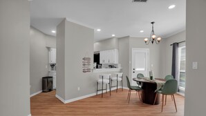 A modern kitchen with white cabinets, a dining area with a wooden table and chairs, and a chandelier. - 4 Bedroom House with Fast Wifi, Game Room, Fireplace, 2 King Beds, Grill, Office (Montgomery)