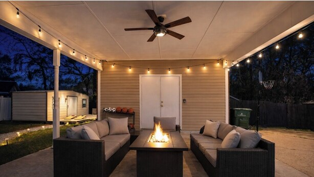 An outdoor patio with a ceiling fan, string lights, a fire feature, and wicker furniture. - 4 Bedroom House with Fast Wifi, Game Room, Fireplace, 2 King Beds, Grill, Office (Montgomery)