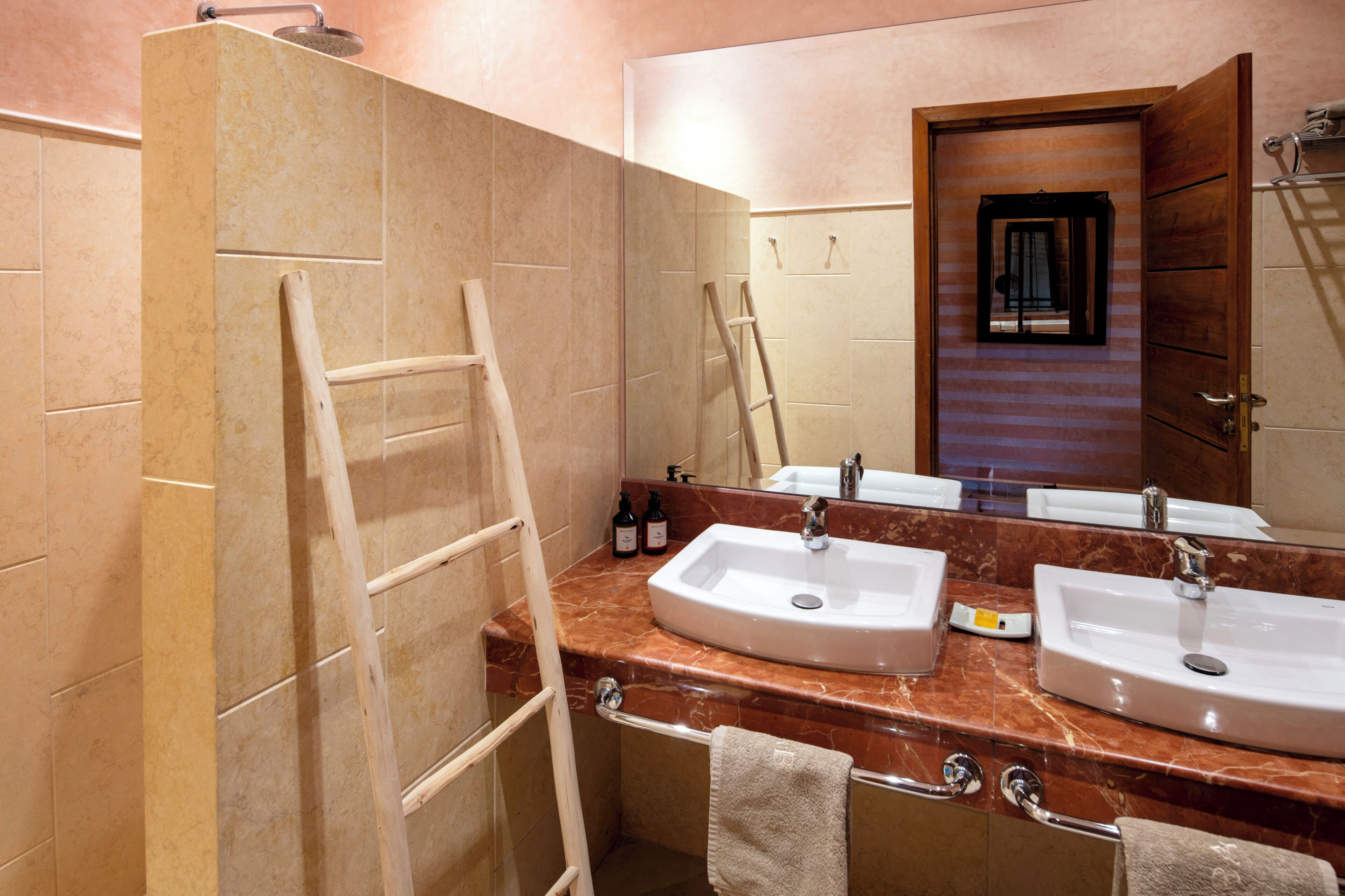 A bathroom with two sinks, a mirror, a towel rack, and a wooden ladder.