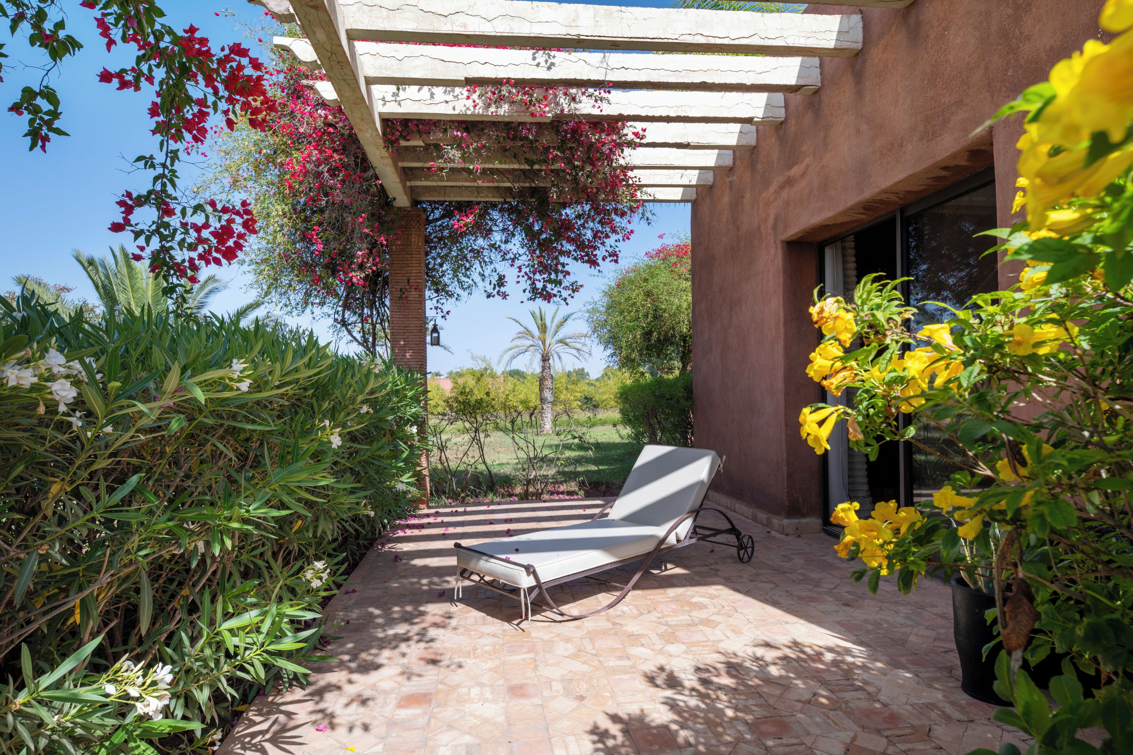 A patio with a lounge chair, a pergola with flowers, and a brick wall.