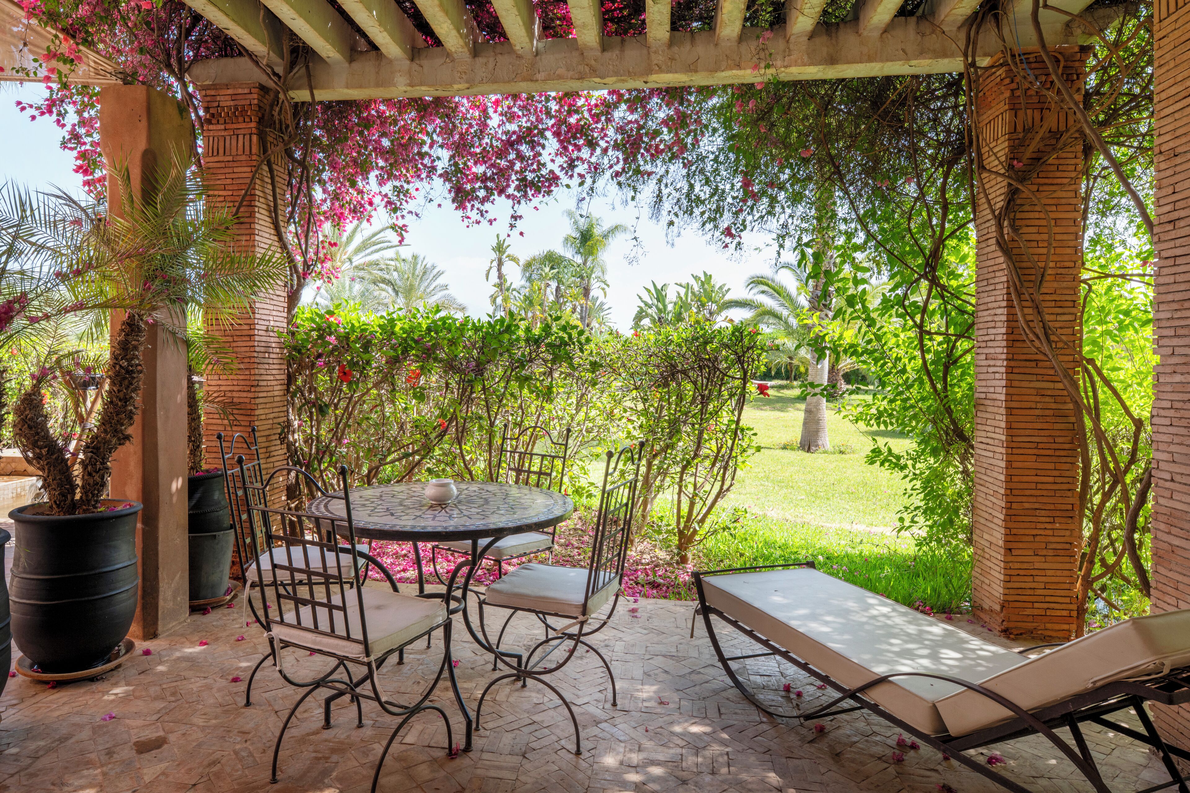 Un patio exterior con una mesa redonda, sillas y una tumbona.