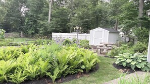Een tuin met een tuinhuis, bankjes en verschillende planten.