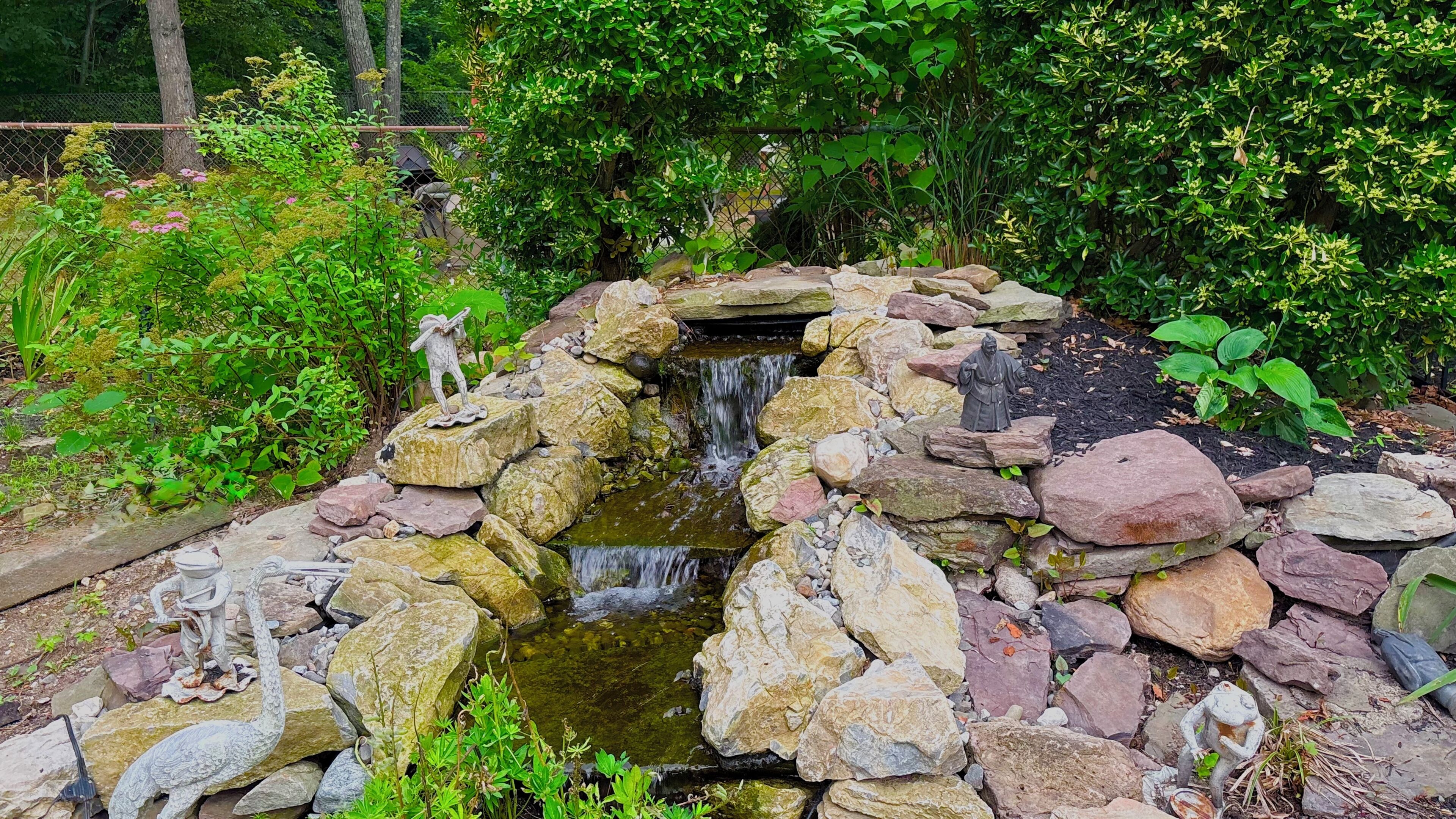 A garden with a small waterfall, rocks, and statues.