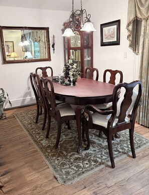 A dining room with a round table, six chairs, a chandelier, a clock, and a mirror on the wall. - Peaceful 3BR Garden Cottage Long Island Escape (Coram)