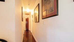 Un couloir aux murs ornés d’œuvres d’art encadrées, avec un plancher en bois et une porte au fond.